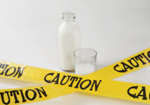 milk bottle and glass next to a caution sign-Lactose Intolerance
