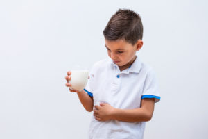 Little boy with dairy allergy holding glass of milk indoors/ airy products