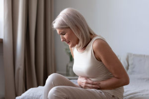 Middle-aged woman sitting on bed feels unhealthy touch stomach suffers from severe crampy abdominal pain, caused by indigestion