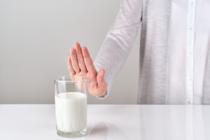 stop sign to glass of milk from woman on white and gray background -lactose intolerance