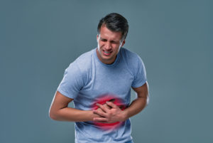 A man touching his stomach, on gray background with copy space. Stomach pain and others stomach disease concept.