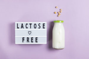 Lettering lactose free on white board with alternative plant milk for vegans in glass bottle against pink background