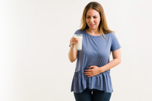 Upset young woman trying to drink a glass of milk.