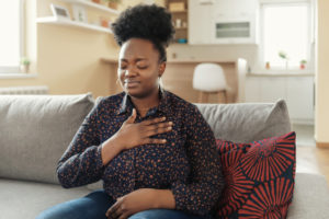 A woman sitting on the couch holding her chest due to discomfort from heartburn.