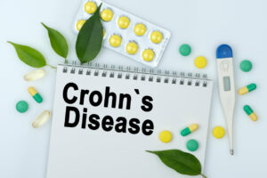 On the table are pills, a thermometer, leaves, and a notebook labeled Crohn's Disease.