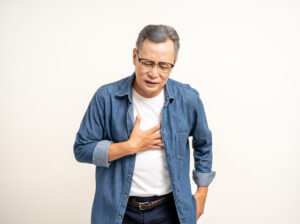 A senior man is experiencing an heartburn and held his hand and squeezed it.